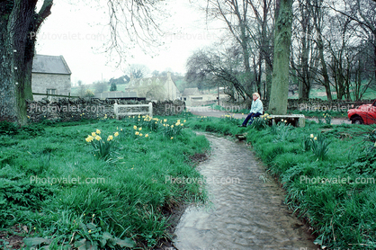 Woman sits in a bucolic setting, Brook, Stream, Burford, Cotswold Hills, Oxfordshire, England