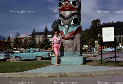 Woman Poses in front of a Totem Pole, cars, 1950s