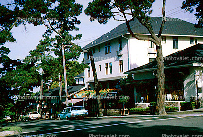 Stores, cypress trees, cars, building, downtown Carmel, 1960s