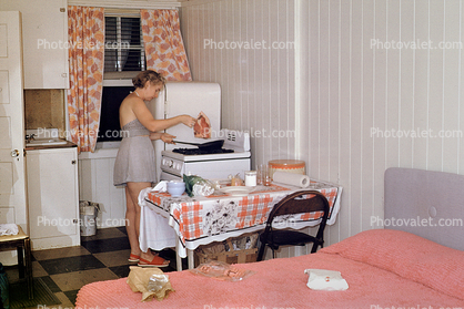 Woman, cooking, frying pan, steak, meat, table, cottage, stove, bed, motel room, 1950s
