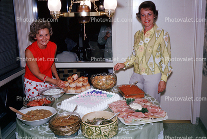 Women with a table of food, ham, cake, smiles, October 1964, 1960s