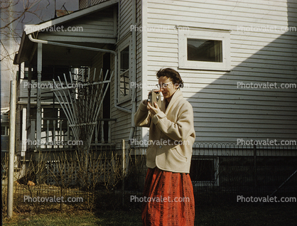 Woman filming with 8mm camera, dress, coat, cold, 1950s