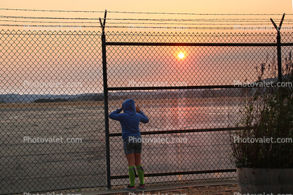 Boy peers into the yonder, sunset, fence