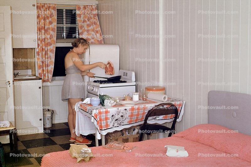 Woman, cooking, frying pan, steak, meat, table, cottage, stove, bed, motel room, 1950s