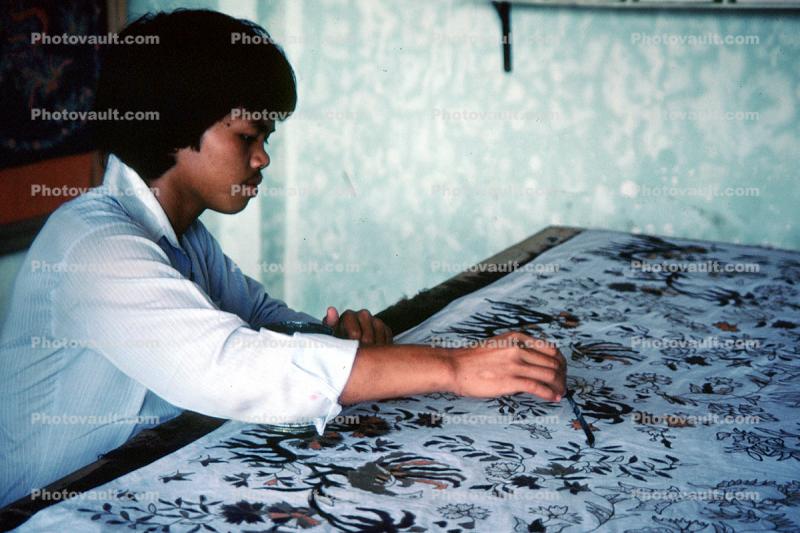 Man painting patterns on a rug, brush