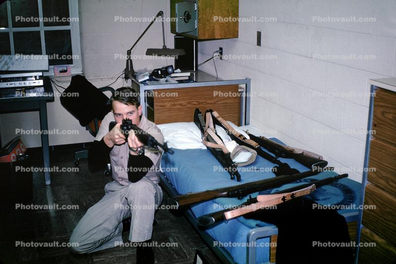 Man aiming rifle in his room, bed, guns, March 1970, 1970s