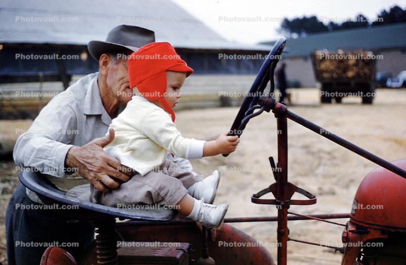 Grandpa teaches grandson to drive tractor, January 1960, 1960s