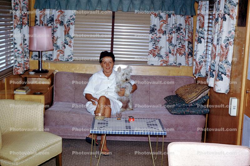 Woman sits on a Sofa, couch, lamp, coffee table, mod, Dog, lampshade, Trailer Home, curtains, 1960s