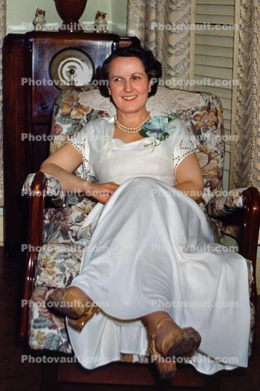 Woman sits, formal dress, smiles, corsage, 1940s