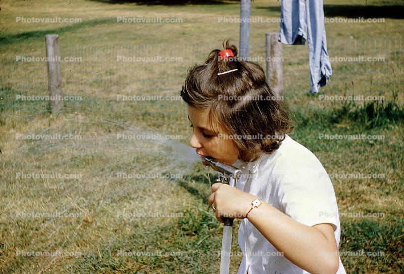 girl drinking water from a hose, 1950s