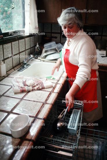 Woman loading dishwasher, kitchen sink