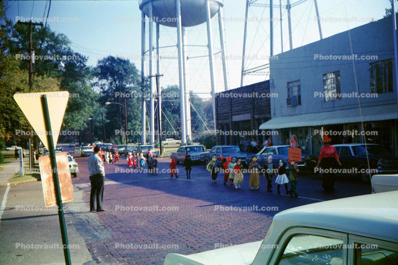 Cars, Chidren in a small parade, buildings, 1950s