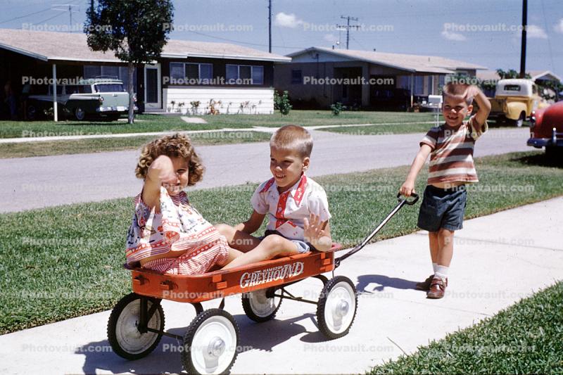 Greyhound pull wagon, boy, girl, brother, sister, sidewalk, suburban, suburbia, cars, 1960s
