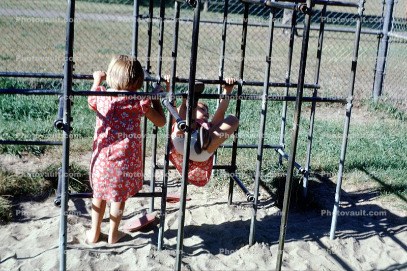 sand, jungle gym, dress, hanging, shadow, sunny, outdoors, outside, exterior, 1950s