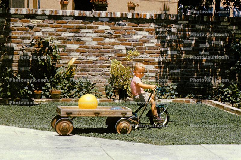 Backyard, tricycle, brick fence, wooden Delux wagon, boy, July 1961, 1960s