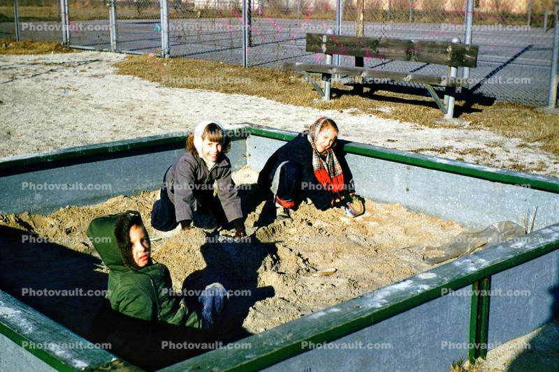 Girls playing in a sandbox, winter, cold, coats, 1950s