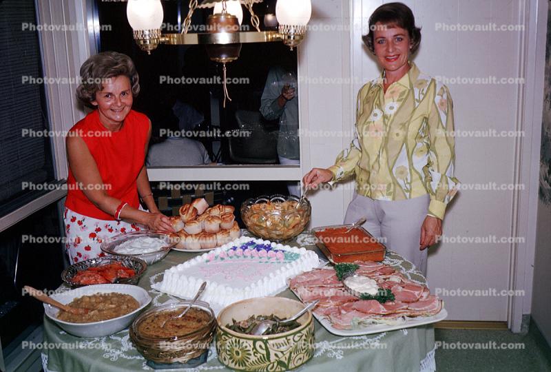 Women with a table of food, ham, cake, smiles, October 1964, 1960s