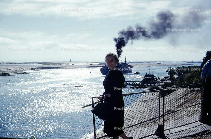 Woman watches a ship cruise y, smoke, 1950s
