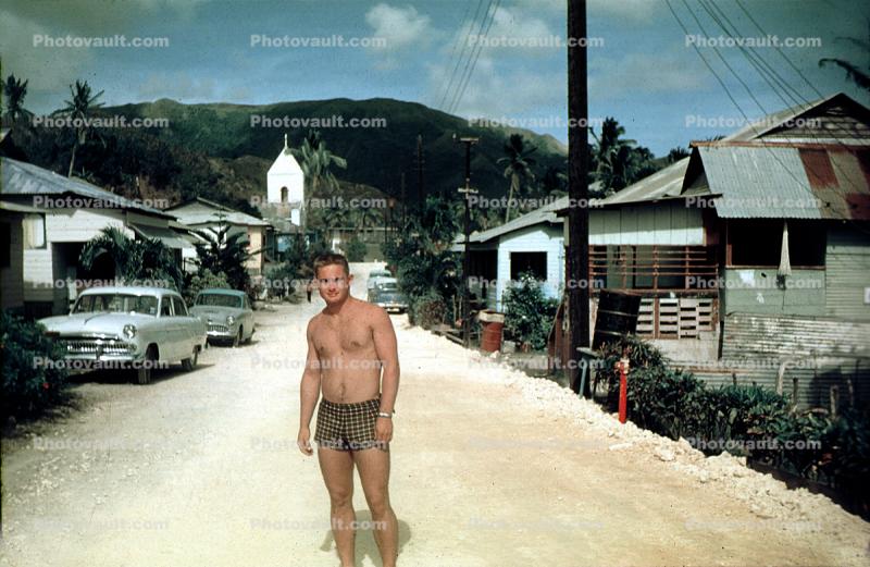 Man stands on a dirt road, street, cars, 1950s