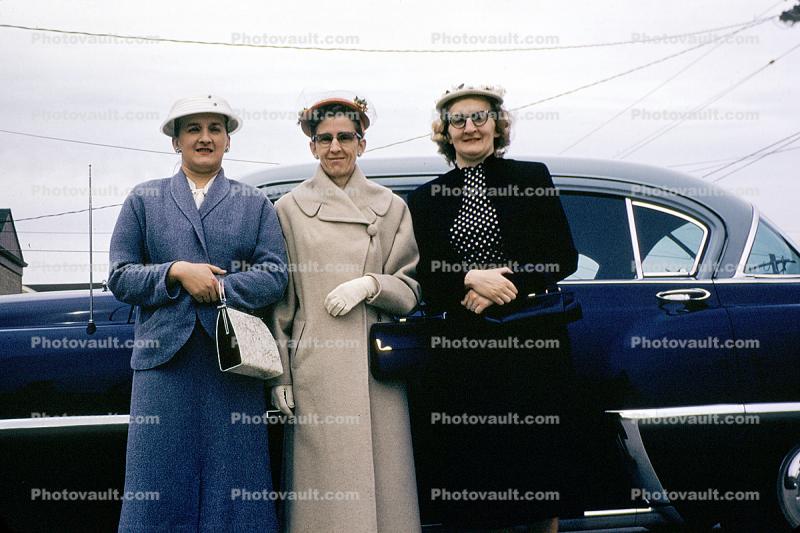 Woman standing in front of a Chevy Car, coats, glasses, purse, cold, 1950s