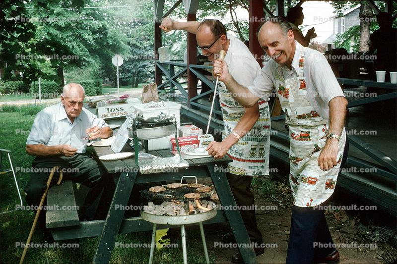 Men, BBQ burgers, picnic table, aprons, July 1975, 1970s