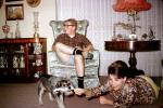 Terrier, living room, woman playing with dog, man sitting, seat, drapes, lamp, 1960s