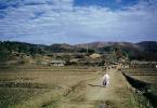 Woman walking down the road, hills, buildings, town, village, near Pusan, South Korea, 1952, CAKV01P01_19