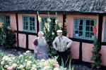 Woman and Man in front of their house, thatched roof, flowers, 1950s, Sod, PORV26P10_03