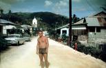 Man stands on a dirt road, street, cars, 1950s