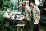 Men, BBQ burgers, picnic table, aprons, July 1975, 1970s