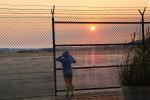 Boy peers into the yonder, sunset, fence